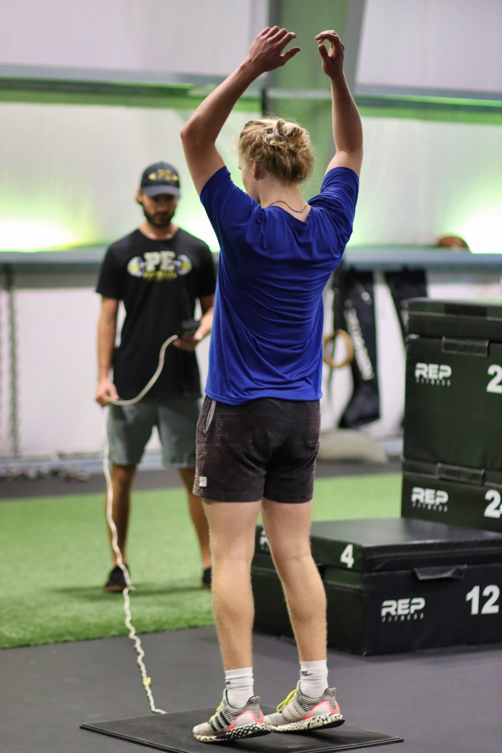 Girl with blue t-shirt and black shorts raising her hands in the gym