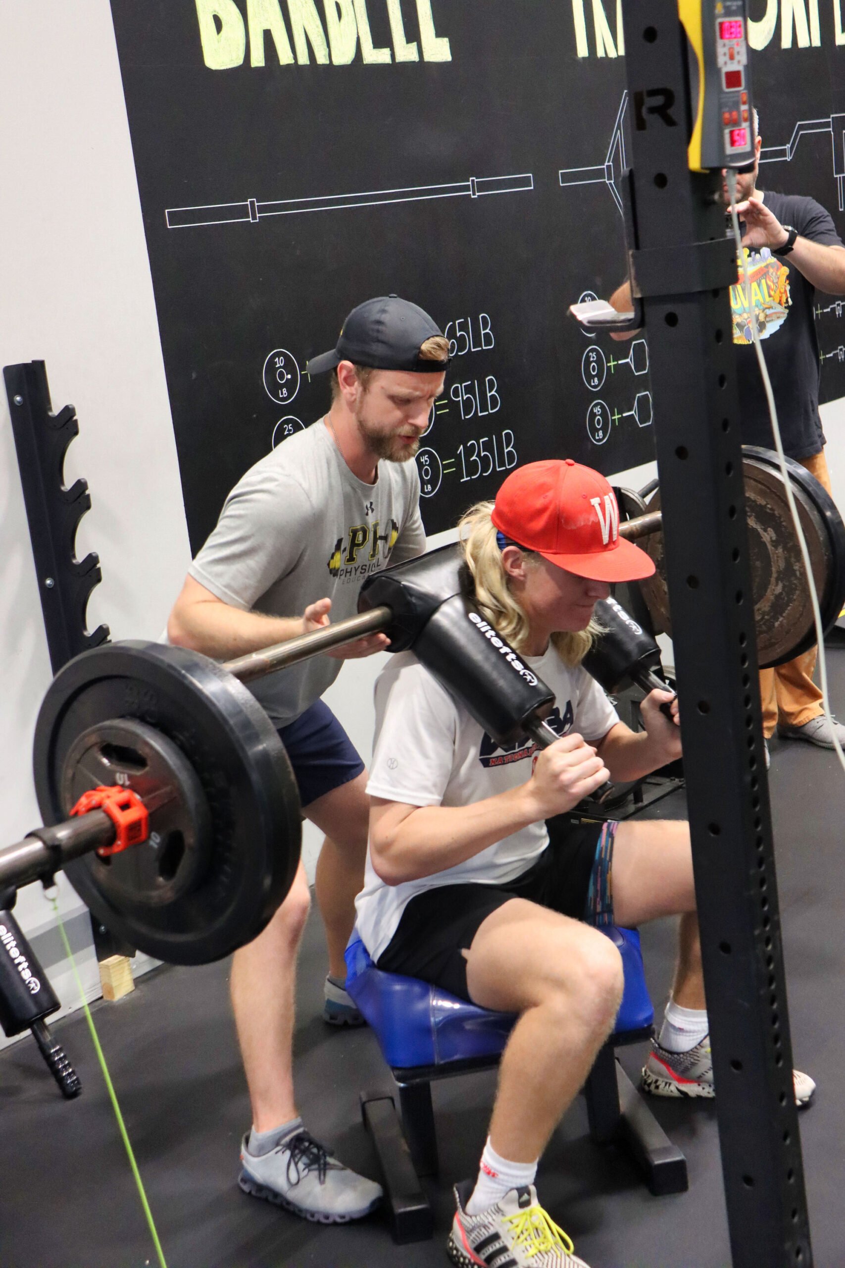 Woman working out with a barbell with the help of her trainer